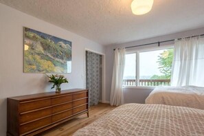 Une chambre à coucher avec un lit, une commode, un tableau et une fenêtre avec des rideaux.