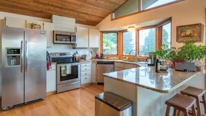 A modern kitchen with wooden ceiling, stainless steel appliances, and a large island with stools. - Tabor Hillside Retreat over the trees, walk to trails, and Montavilla cafes.  (Portland)