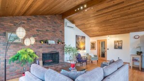 A cozy living room with a brick fireplace, grey sofas, and a wooden ceiling. - Tabor Hillside Retreat over the trees, walk to trails, and Montavilla cafes.  (Portland)