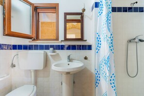Een badkamer met toilet, wastafel, spiegel, douche en betegelde wanden.