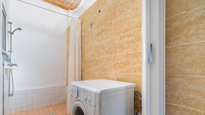 A laundry room with a washing machine, a shower, and a tiled floor.
