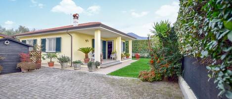 A yellow house with a tiled roof, a small porch, and a paved driveway.
