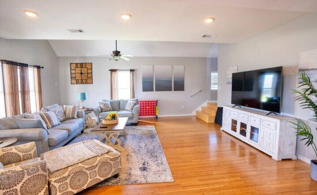 A spacious living room with a large sofa set, a coffee table, and a TV on a white cabinet.