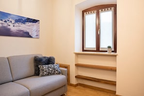 Uma sala de estar com sofá, janela com vista para montanhas e um quadro na parede.