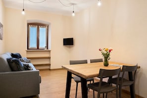 Uma sala de estar com sofá, mesa de jantar com cadeiras, televisão na parede e janela com cortinas.