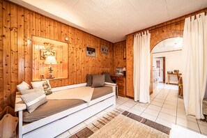 Une pièce aux murs lambrés, avec un lit, une lampe et un coin repas visible à travers une arche.