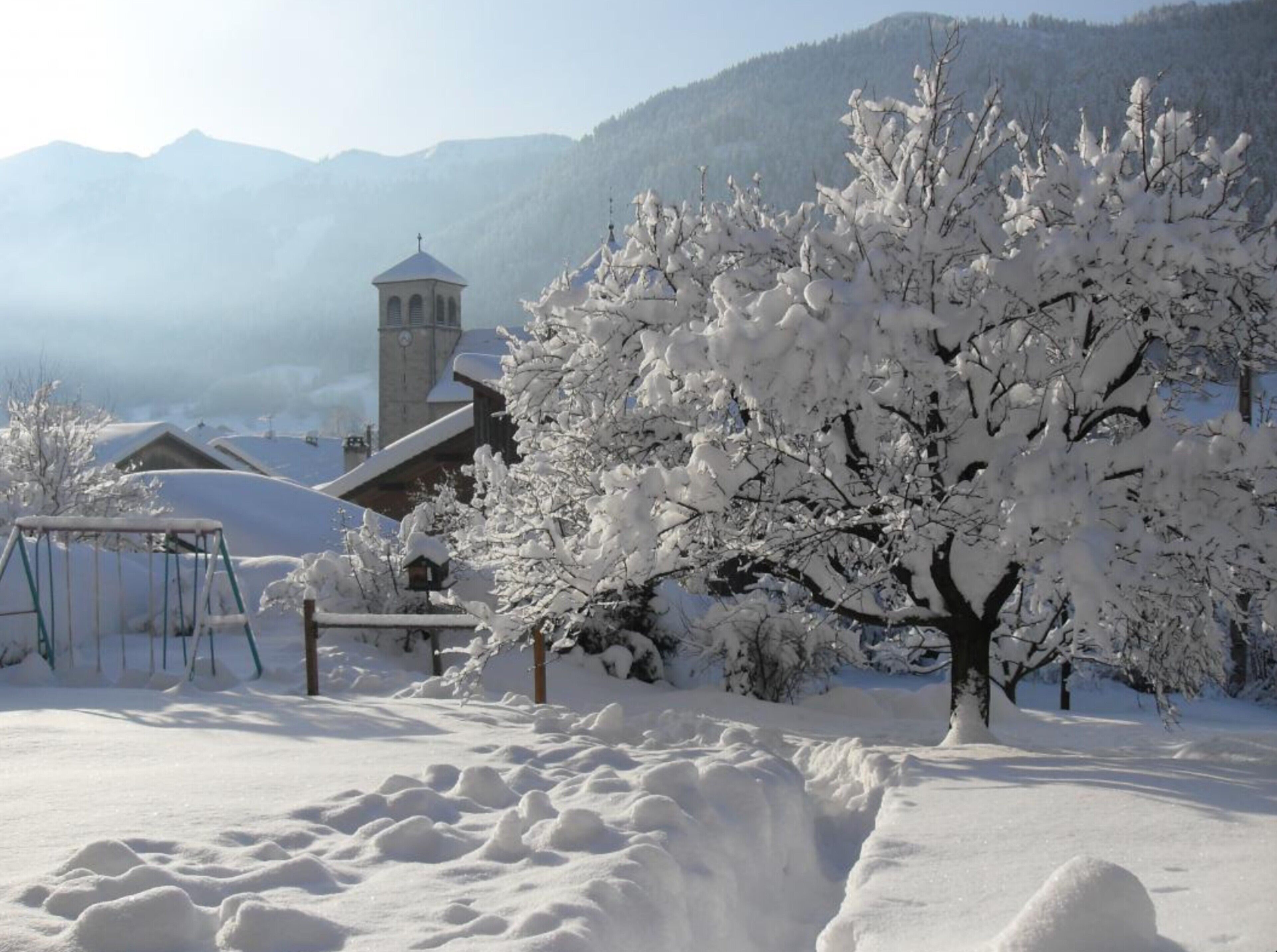 Paisaje nevado con una iglesia, un columpio y un árbol cubierto de nieve.