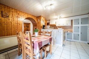 Puisesti sisustettu tila, jossa on ruokapöytä, tuoleja ja keittiö, jossa on kaappeja.