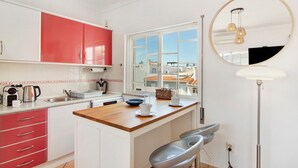 Une cuisine avec des meubles de couleur rouge et blanche, un plan de travail en bois, une fenêtre avec vue et un miroir rond agrémenté de luminaires suspendus.