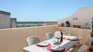 Un balcon avec une table dressée pour deux personnes, des chaises, une lampe et une vue sur la mer.