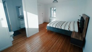 Een slaapkamer met een houten vloer, een bed met beddengoed met een patroon, een raam en een deur naar een badkamer.