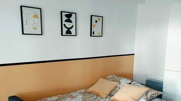 A single bed with a floral-patterned duvet, a black bench, and three abstract wall art pieces.