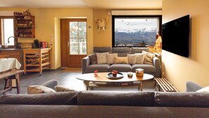 A living room with a sofa, a coffee table, a bookshelf, a television, and a window with a mountain view. - Apartment "Le Pacardou" with Mountain View, Private Terrace and Wi-Fi (Saint-Gervais-Les-Bains)