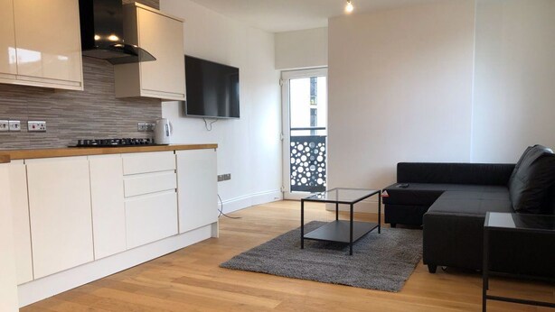 A modern kitchen with white cabinets, a black countertop, and a built-in stove. There is a black sofa and a small table in the living area. -  Hull Spacious Apartment 7 (Hull)