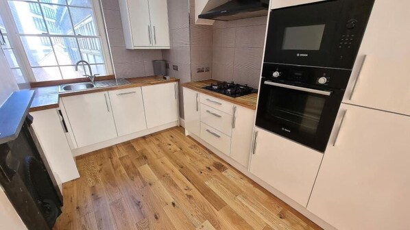 Una cocina con armarios blancos, encimera de madera, horno Bosch y ventana que deja entrar luz natural.