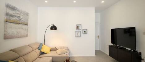Una sala de estar moderna con un sofá, una mesa de centro, una lámpara de pie, un televisor de pantalla plana y un cuadro en la pared.