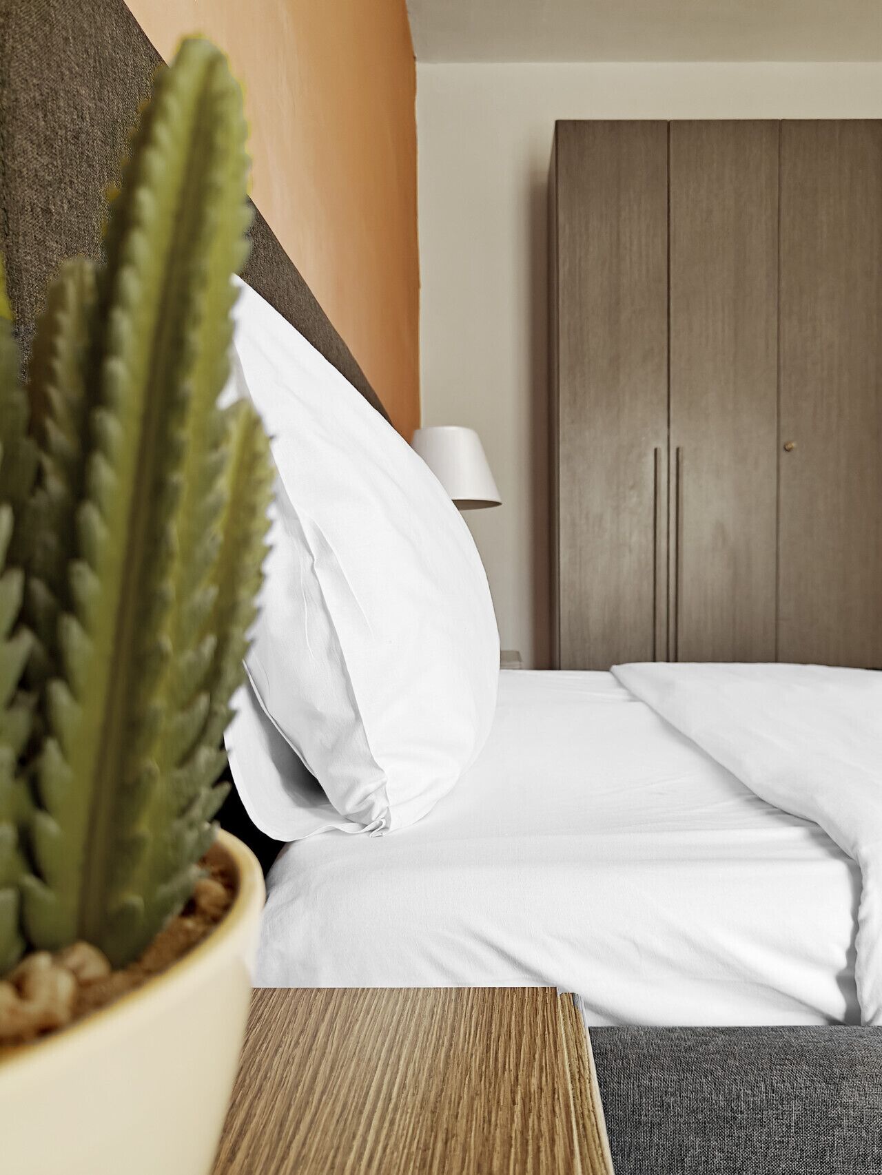 Ein Hotelzimmer mit Bett, Zimmerpflanze, Holzschrank und Nachttischlampe.
