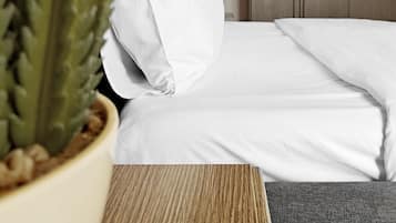 Une chambre d’hôtel avec un lit, une plante en pot, une armoire en bois et une lampe de chevet.