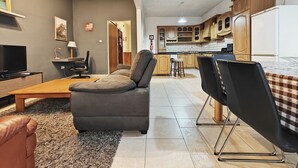 En stue med sofa, fjernsyn, lampe og et køkken i baggrunden.