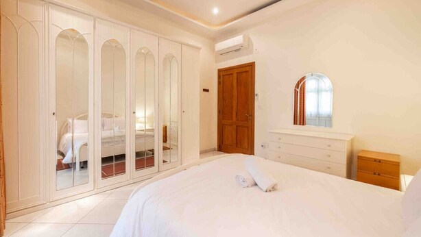 A bedroom with a large bed, a wardrobe with mirrored doors, a wooden door, a dresser, and a mirror. - 2 bedroom by Sliema promenade (Tas-Sliema)