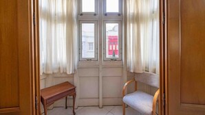A room with a wooden bench and a chair, a double door with windows, and a view of a red building outside. - 2 bedroom by Sliema promenade (Tas-Sliema)