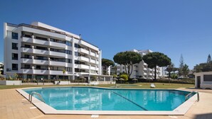 A swimming pool with a tiled deck, surrounded by a white building with multiple balconies and a clear blue sky. - Apartment 'Tenis Golfmar' with Shared Pool, Wi-Fi and Air Conditioning (Vialmoura)
