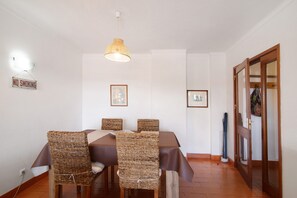 Un comedor con sillas de mimbre, una mesa con mantel marrón, una lámpara colgante y un cartel de 'No Smoking'.