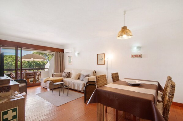 Una habitación con una mesa de comedor, sillas, un sofá, un televisor y un balcón con vistas.