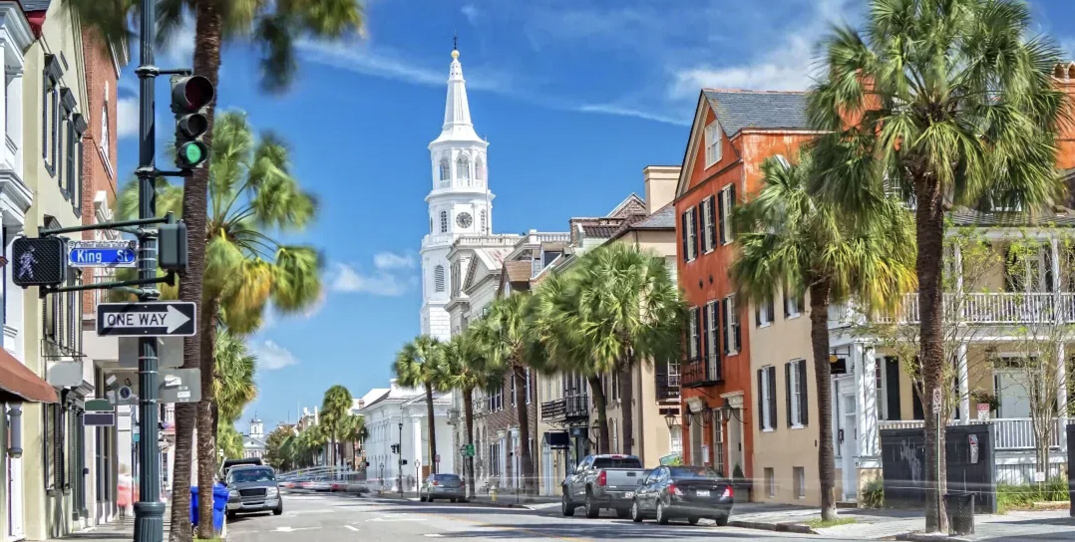 A street with palm trees, a church with a steeple, and buildings with balconies.