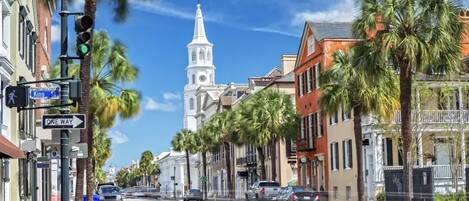 A street with palm trees, a church with a steeple, and buildings with balconies.
