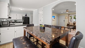 A modern kitchen with white cabinets, a marble island, and a dining area with leather chairs.