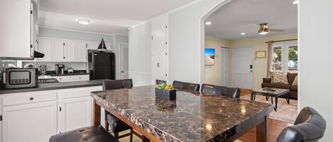 A modern kitchen with white cabinets, a marble island, and a dining area with leather chairs.