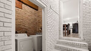 A laundry room with two washing machines and a dryer, adjacent to a staircase leading to a kitchen area.