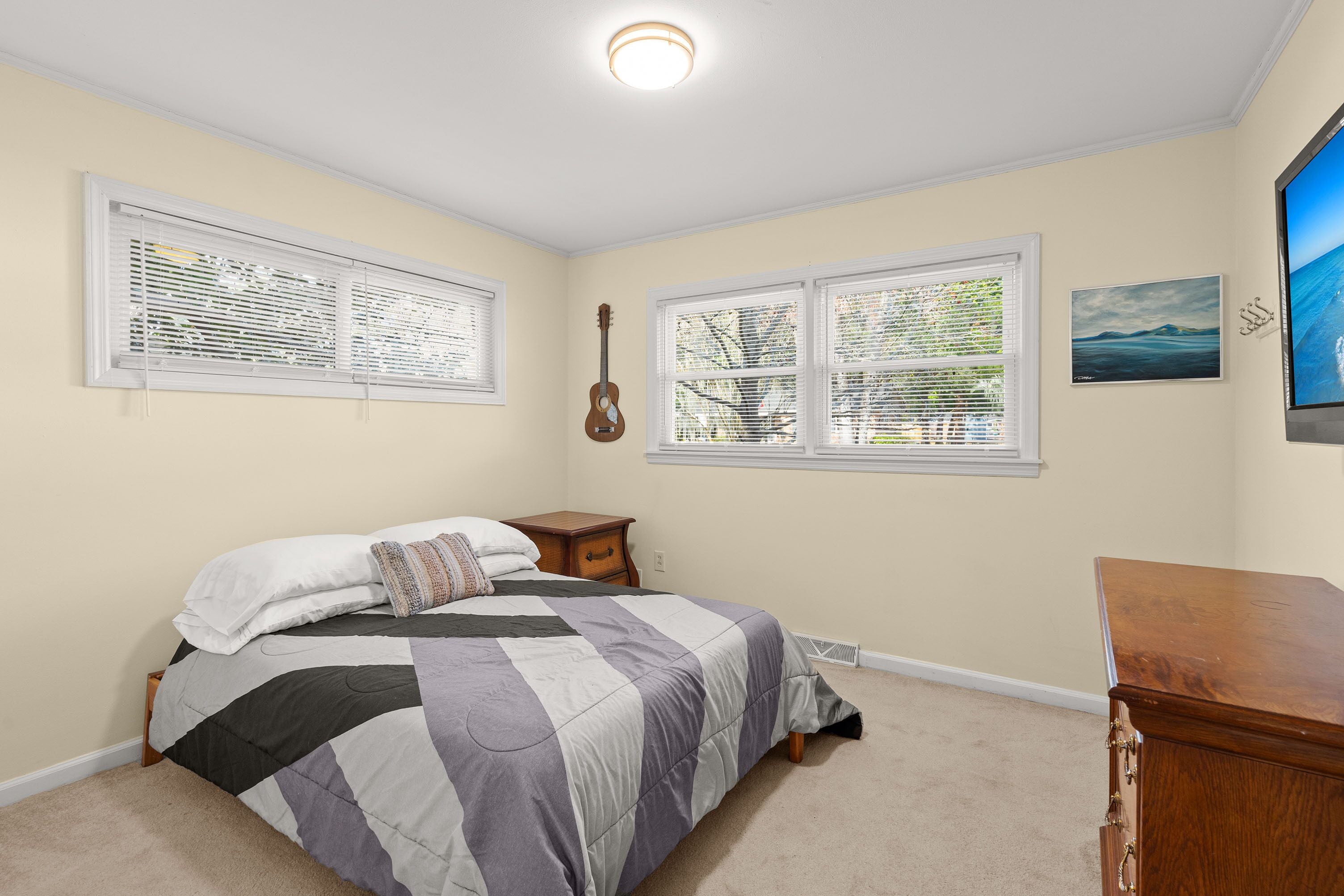 Un dormitorio con una cama, una guitarra, un aparador y dos ventanas con persianas.