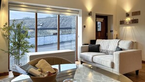 A living room with a sofa, a glass coffee table, a plant, and a view through large windows. - 1 bedroom accommodation in Falmouth (Falmouth)