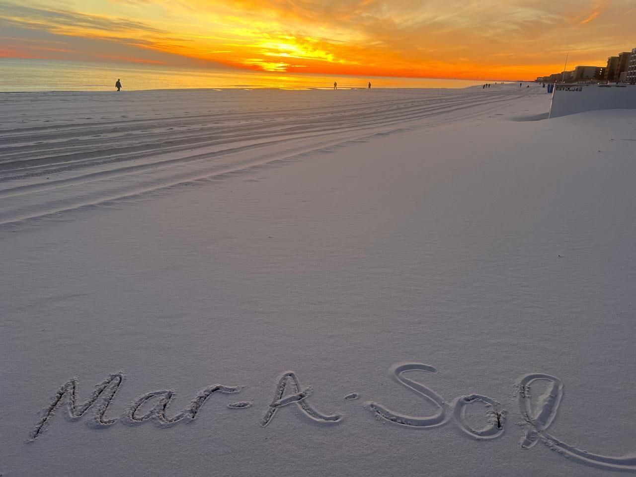 Una playa con huellas que deletrean "Mar-A-Sol" y un cielo despejado.