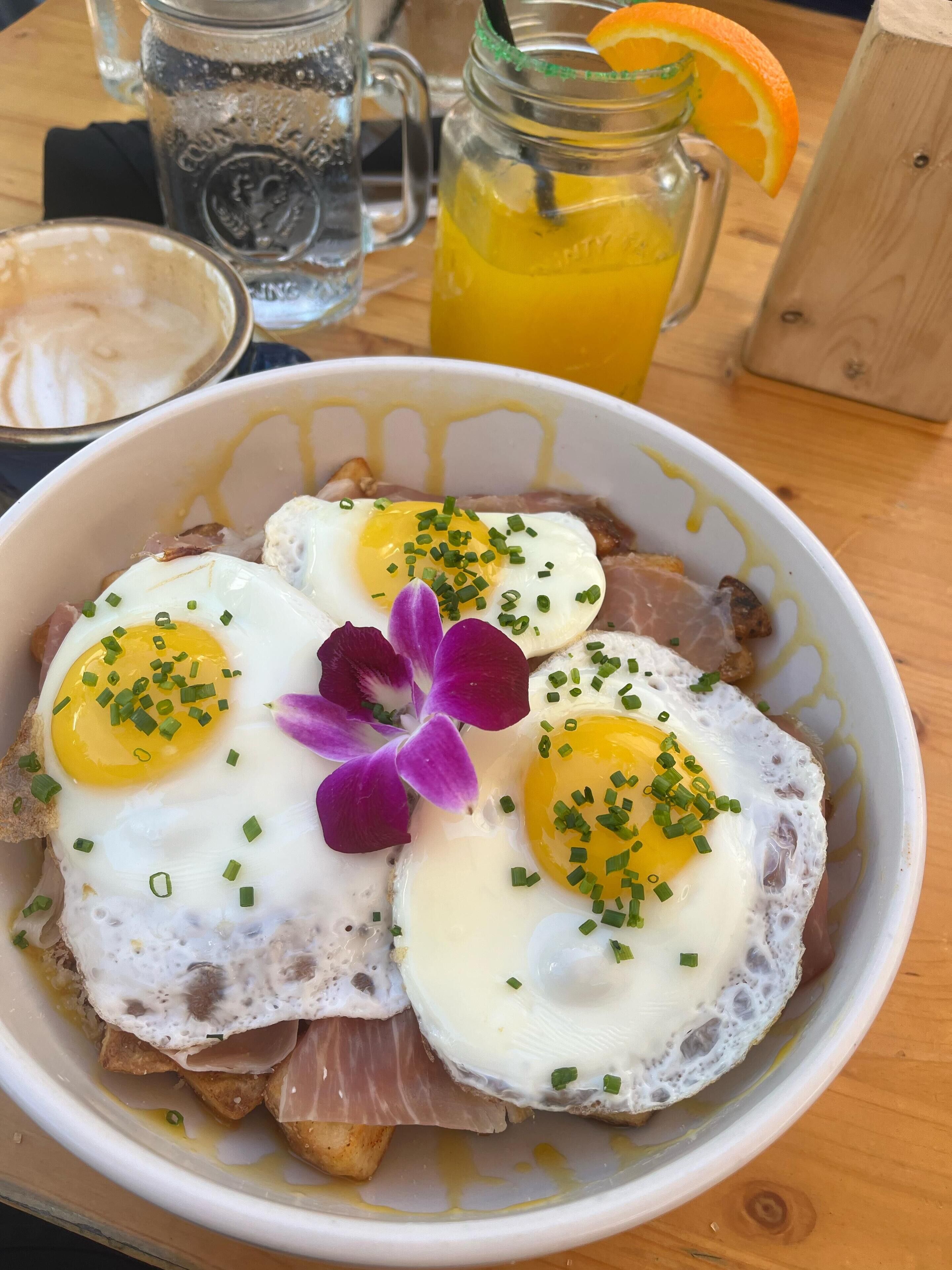 A bowl of food with eggs, green onions, and a purple flower garnish.