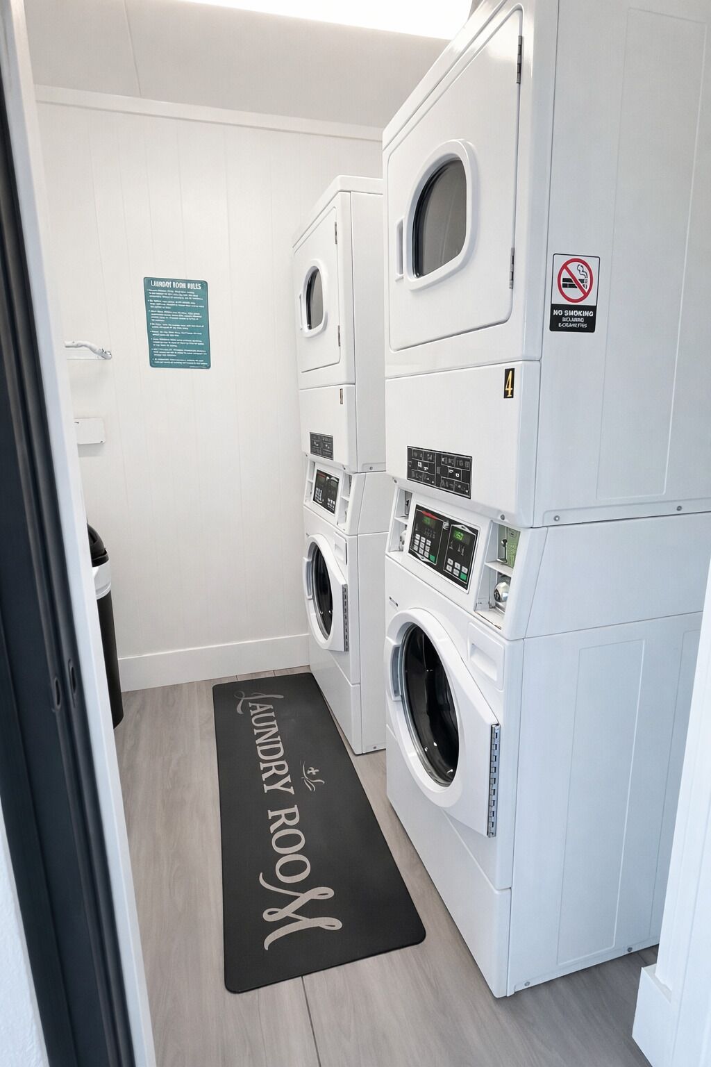 A laundry room with two front-loading washing machines, a no-smoking sign, and a sign detailing laundry room rules.