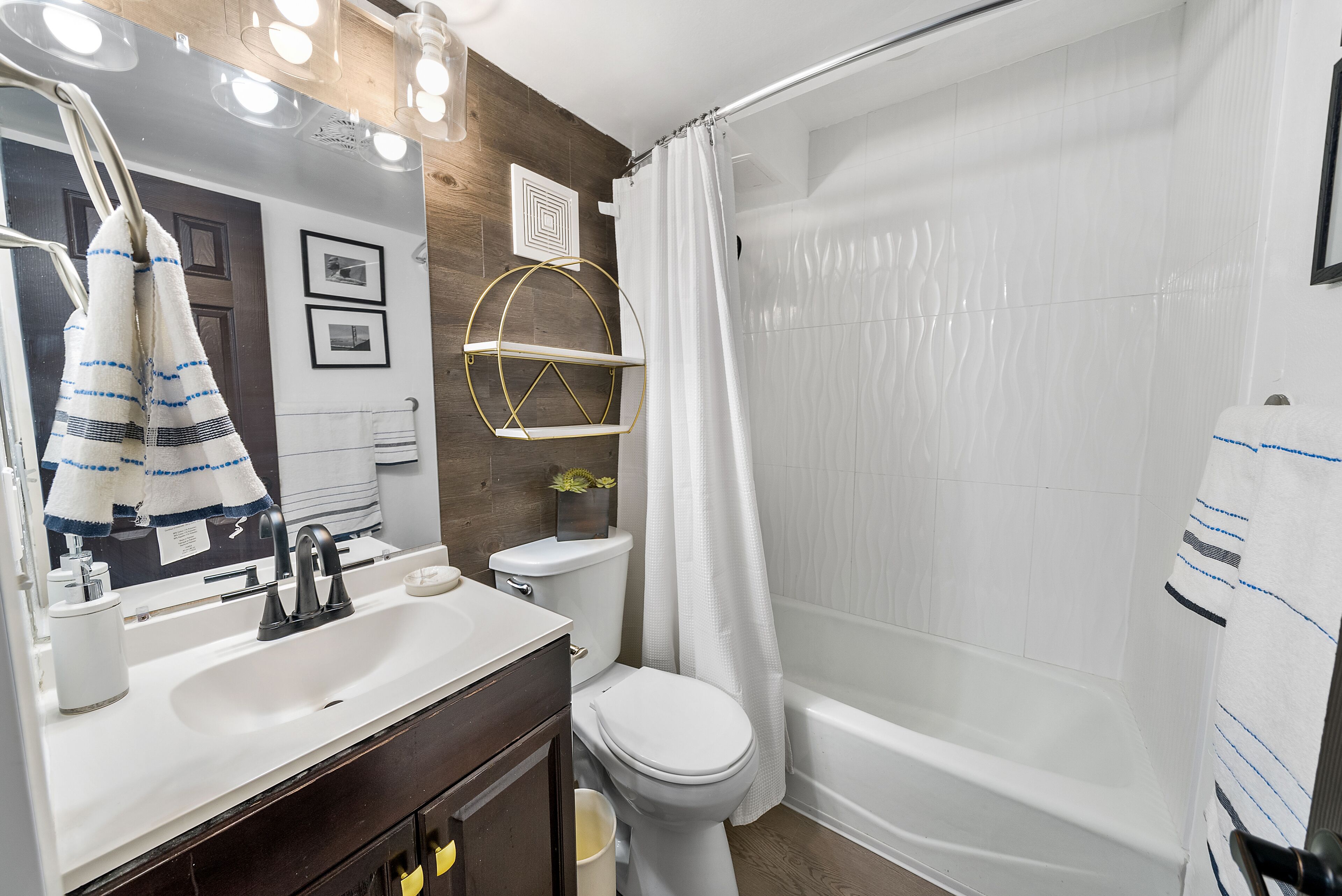 Ein modernes Badezimmer mit einem weißen Waschbecken, einer Toilette und einer Badewanne. Handtücher hängen an der Wand und eine Duschvorhang ist angebracht.