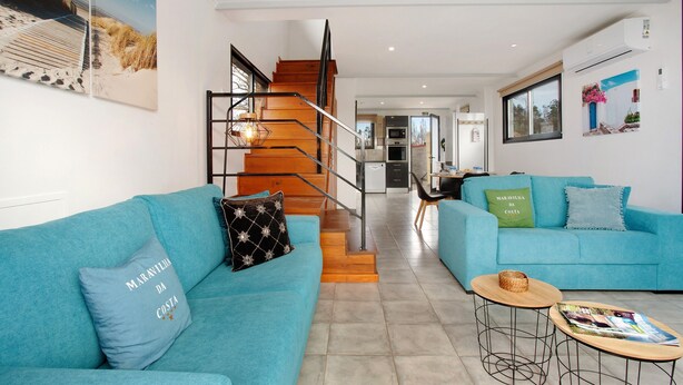 Un salon moderne avec un escalier, deux canapés, une table basse et une cuisine en arrière-plan.