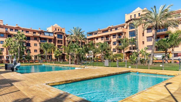 Een resort met twee zwembaden, palmbomen en een houten terras.
