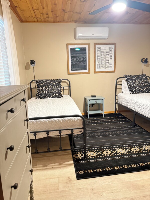 A bedroom with two beds, a dresser, a small table, and an air conditioning unit on the wall. - Comfy, Cozy Cabin in the Mountains with a large front porch. Pet-Friendly! (Heber-Overgaard)
