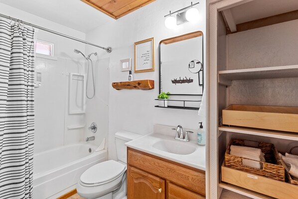 A bathroom with a bathtub, toilet, and shower. There are wooden shelves with towels and a framed quote on the wall. - Comfy, Cozy Cabin in the Mountains with a large front porch. Pet-Friendly! (Heber-Overgaard)