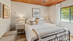 Een slaapkamer met een houten plafond, een bed met witte lakens, twee nachtkastjes met lampen en een raam met jaloezieën.