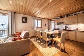 Un salon chaleureux avec un canapé, une table à manger et des chaises, un plafond en bois et un coin cuisine équipé de placards et d’une fenêtre.