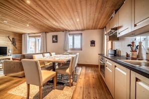 Une cuisine moderne avec des meubles en bois, un coin repas avec une table et des chaises, et un espace de vie chaleureux avec un canapé et une télévision.