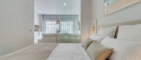 Una habitación de hotel moderna con una cama grande, un separador de vidrio, un área de comedor y vistas a la ciudad.