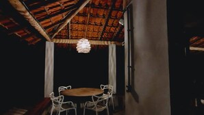 A dimly lit room with a wooden ceiling, a round table with chairs, and a hanging light fixture. - Casa do Rio, Rio Bonito de Lumiar (Lumiar)