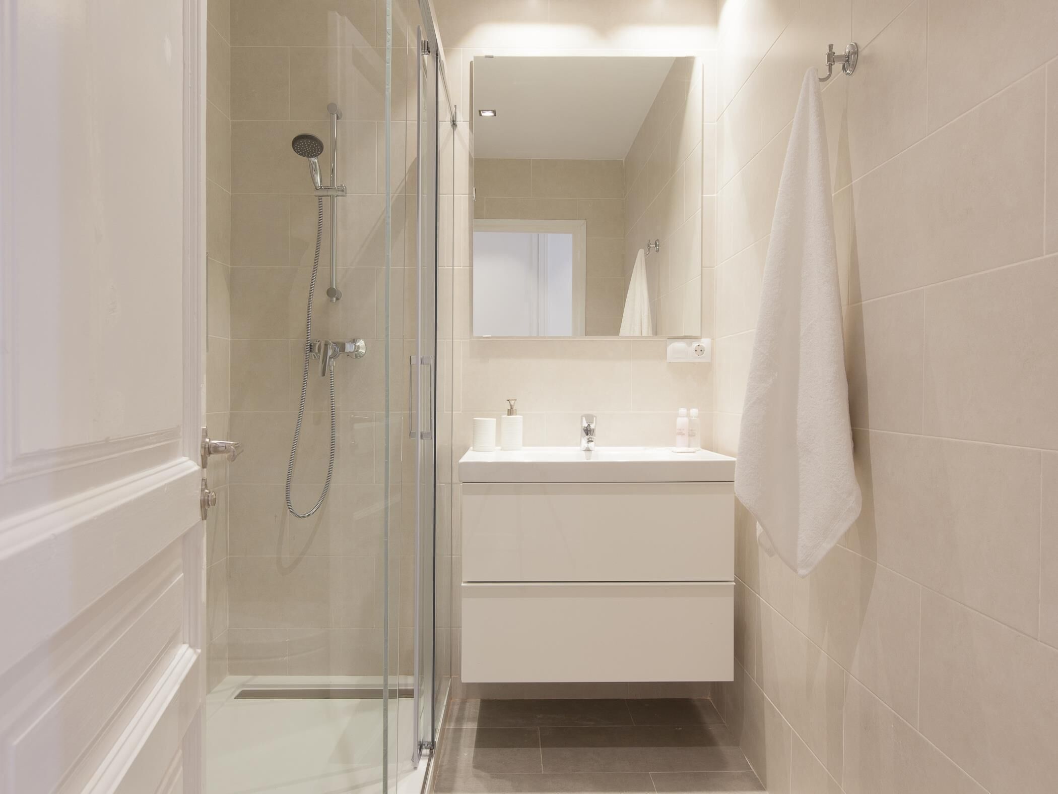A modern bathroom with a glass-enclosed shower, a white vanity with a mirror, and a towel hanging on the wall.