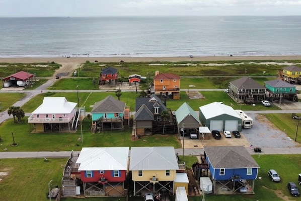 A coastal residential area with houses, some elevated on stilts, and a beach in the background.